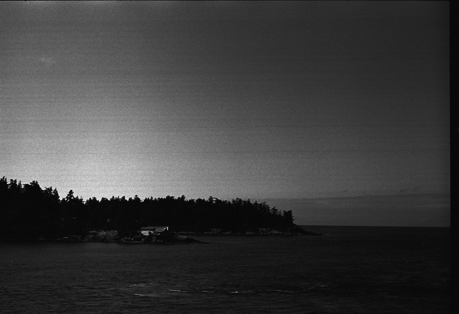 A low wooded islet reduced to a black band between bright water and a luminous overcast sky.