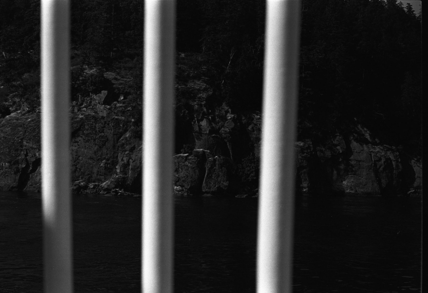 Three vertical bars of light fall across a rocky shoreline, a light leak burned into the negative.