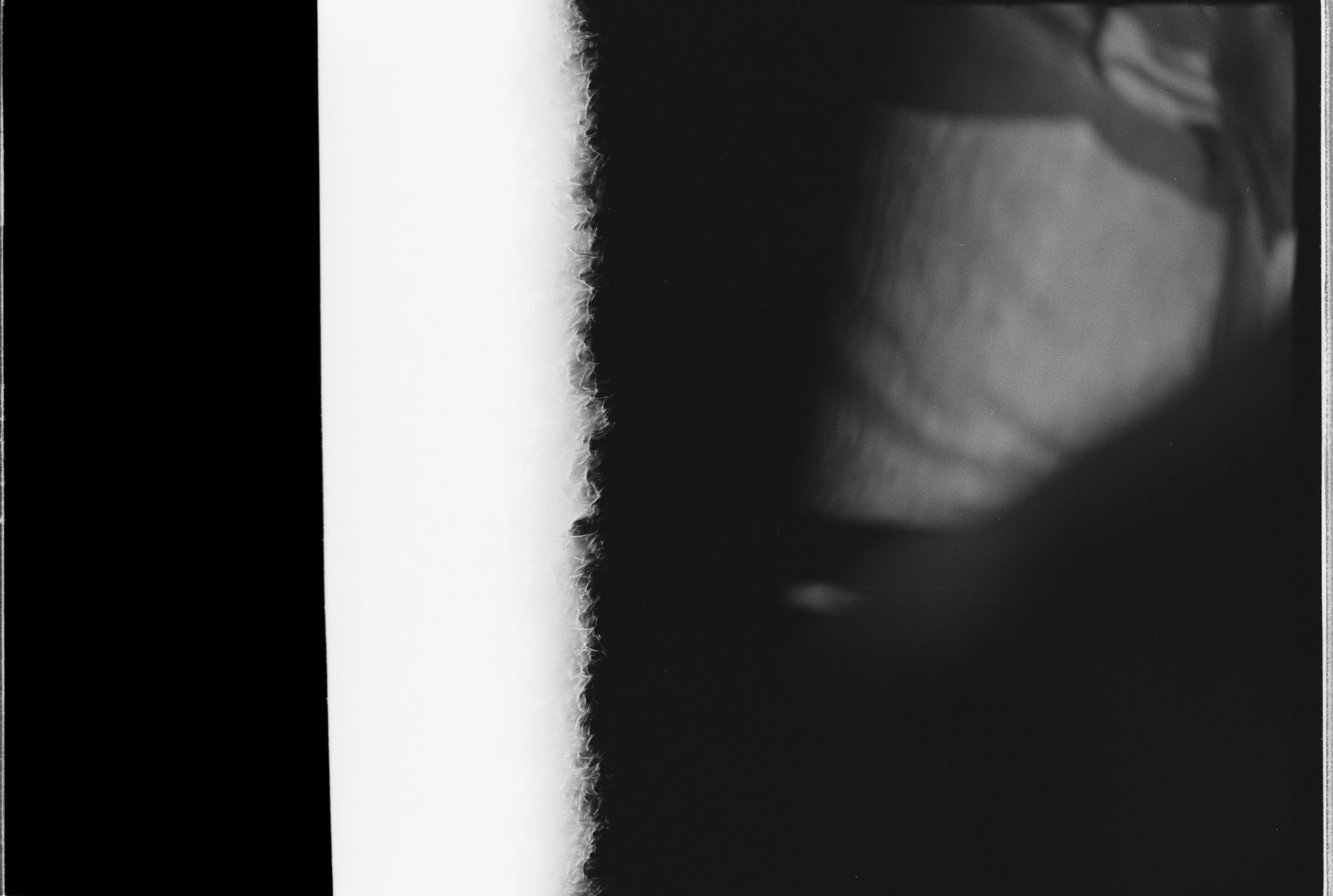 The light-struck head of the roll: a solid black bar, a fogged edge where the film met daylight, and a faint unresolved shape.